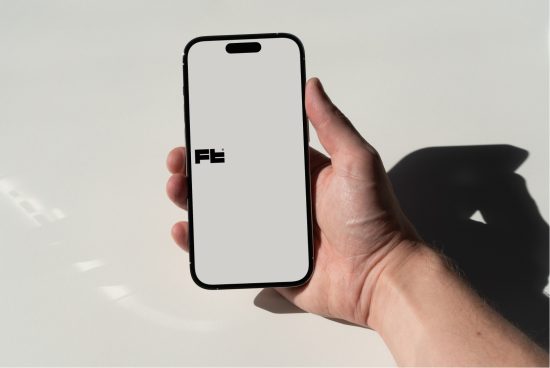 Hand holding smartphone mockup with blank screen for app design presentation, displaying shadow on white surface, suitable for graphics and templates.